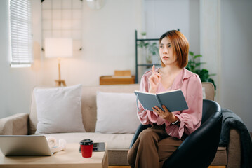 Young woman sits comfortably on a sofa, reading a notebook while holding a coffee cup.