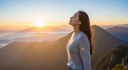 Young Asian woman with eyes closed breathing in fresh mountain air at sunrise