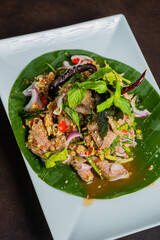 Delicious and vibrant Thai dish beautifully presented on a green leaf and a white plate. The dish is a culinary delight, inviting a sensory experience.
