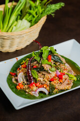 A close-up shot of a plate of delicious Thai food. The dish is garnished with fresh herbs and spices, and served with a basket of fresh vegetables