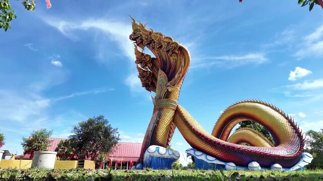 Golden naga statue outdoor sculpture temple under blue sky with multiple serpent heads surrounded by green grass bright day cultural grandeur serenity