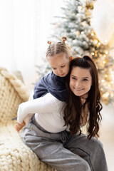 Obraz premium A mother and daughter share a loving moment during the Christmas season, with a decorated tree in the background.