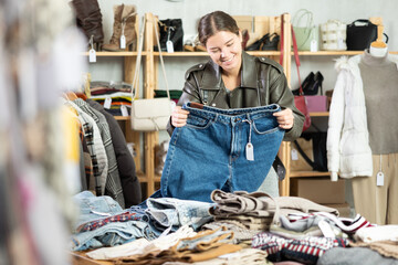 Happy young girl choosing jeans trousers in clothing shop with new winter collection