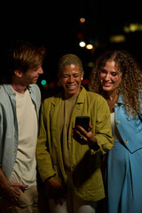 Diverse friends laughing watching smartphone outdoor at night