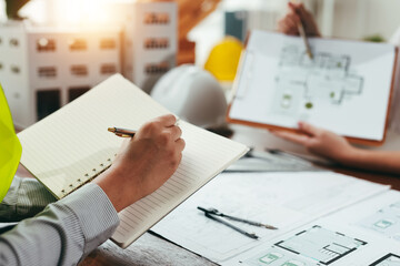 Engineers collaborating on a construction project, discussing blueprints and architectural plans while writing notes in a meeting