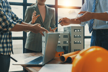 Architects and engineers collaborating, discussing a building model over a table with laptop and blueprints in a sunny office