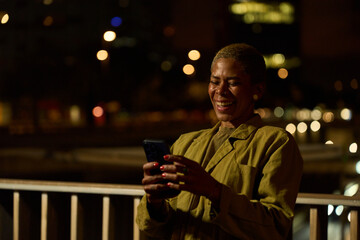 Woman smiling using smartphone on urban balcony at night