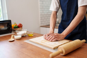 Man wearing an apron kneading dough on a chopping board in a modern kitchen, preparing homemade bread