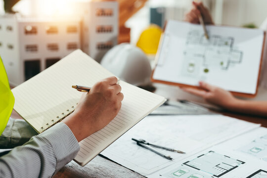Engineers collaborating on a construction project, discussing blueprints and architectural plans while writing notes in a meeting