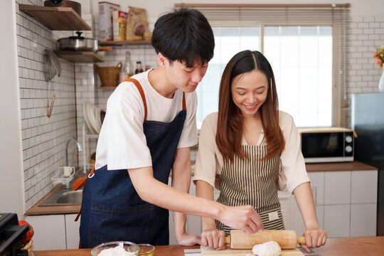 Young Asian couple sharing happy moment preparing homemade baked goods in modern kitchen, enjoying cooking lifestyle together