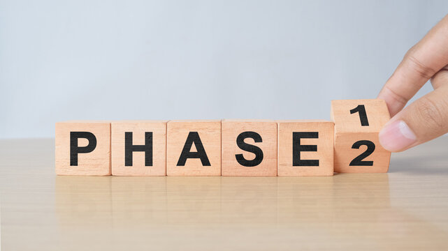 Time for Phase 2. Hand is turning a cube and changes the word 'Phase 1' to 'Phase 2'. Beautiful white background. Business concept