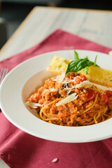A plate of delicious spaghetti with a tomato-based sauce, garnished with basil and parmesan cheese. Served alongside bread