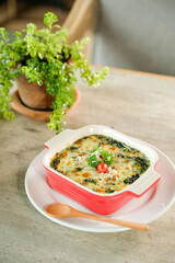 A delicious spinach casserole in a red dish with a wooden spoon and green plant