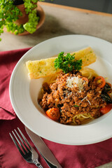 A delicious serving of spaghetti bolognese with a side of garlic bread on a white plate. This mouthwatering meal is garnished with fresh herbs