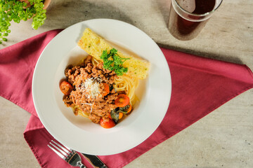 A delicious plate of spaghetti bolognese, served with garlic bread and a drink. The dish is garnished with parsley and parmesan cheese, making it a complete meal