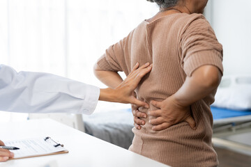 Doctor examining senior woman's lower back, performing a physical check up for back pain during a...