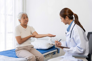 Fototapeta premium Senior woman experiencing elbow pain, consulting with a female doctor who is writing notes on a clipboard in a medical room