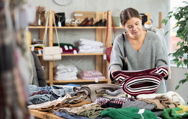 Fototapeta premium Young woman buyer choosing warm sweater in clothing store
