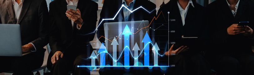 A group of business professionals engage in financial analysis utilizing technology. They observe digital graphs and charts on laptops and smartphones, showcasing data trends. Scalp