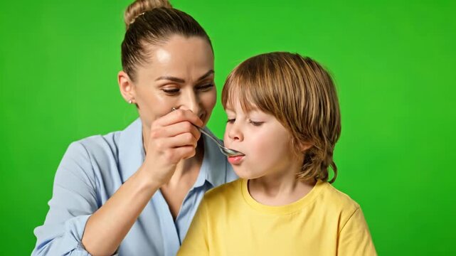 Caring Mother Gives Liquid Medicine to Her Reluctant Son on a Green Screen.
