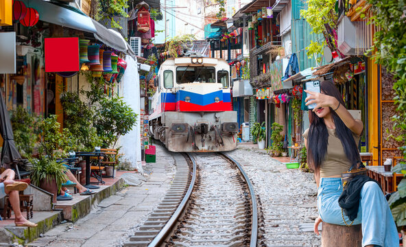 A young and beautiful Vietnamese woman is taking a selfie when an old-fashioned train arrives.