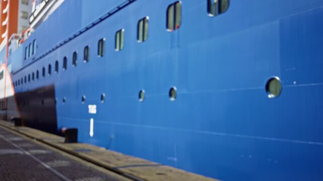 Blue cruise ship hull in shallow blurred bokeh and defocused foreground at dockside outdoor; background backplate copyspace calm.
