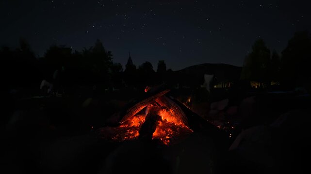 Campfire Burns Brightly at Night, People Gather in Background