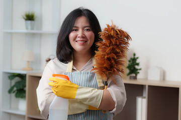 Home Cleaning. A woman smiling while holding cleaning supplies and a feather duster.