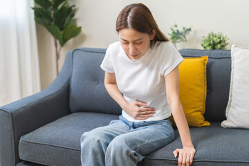 Sick asian young woman in pain, hand holding belly, stomach pain from food poisoning, girl hurt...