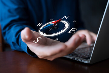 Digital compass floating above businessman's hand with laptop showing navigation and direction...
