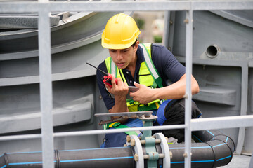 A construction worker at a facility, wearing safety equipment and talking on walkie talkie in the...