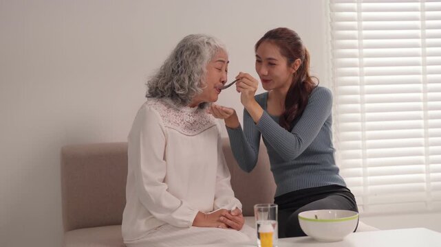 Asian young adult woman provide home care assistance older adult woman senior mealtime support domestic environment generational bonding daily living aid