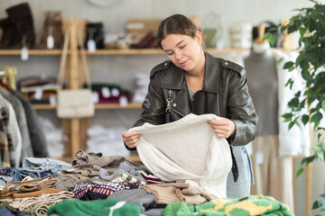 Young female shopper choosing knitted sweater in clothing store