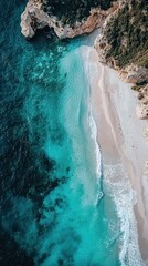 High-angle view of a secluded beach nestled within a rocky cove. Turquoise water laps at a pristine white sand beach.  Waves gently break along the shore
