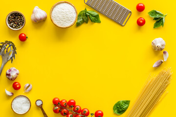 Frame of ingredients for cooking Italian pasta - uncooked spaghetti with tomatoes and basil leaves - on a yellow background, top view