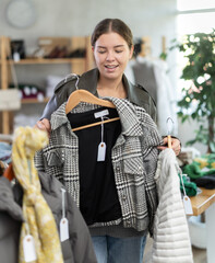 Young female shopper buying winter and autumn outerwear in clothing store