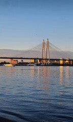 The majestic cable-stayed bridge over the Neva River in Saint Petersburg captured at sunset, creating a warm, golden reflection on the water.