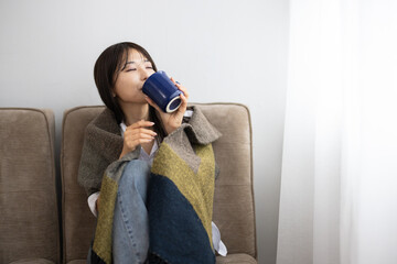 Young Woman Enjoying a Warm Drink Wrapped in a Blanket by the Window
