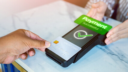 Close-up of customer's hand making payment by tapping credit card. The screen displays the message 