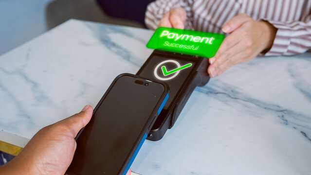 Close-up of customer's hand using smartphone to make successful contactless payment. Phone is tapped on POS terminal with green check mark, showing electronic wallet transaction.