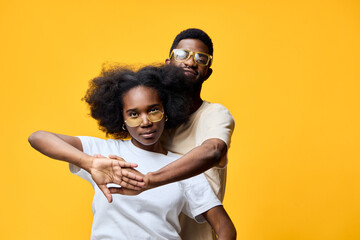 Stylish couple posing against a vibrant yellow background, exuding confidence and joy with casual...