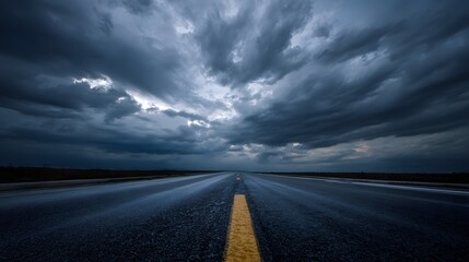Dramatic stretch of empty roadway disappears into dark, ominous storm clouds overhead