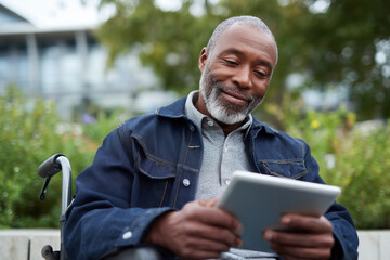 Fototapeta premium A man in a wheelchair is smiling as he looks at a tablet