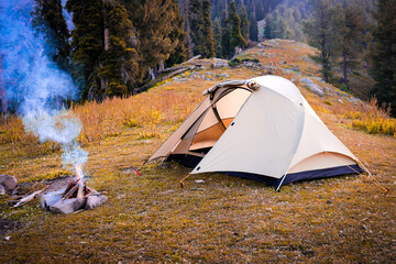 Peaceful camping scene with tent and campfire in mountain forest outdoor wilderness
