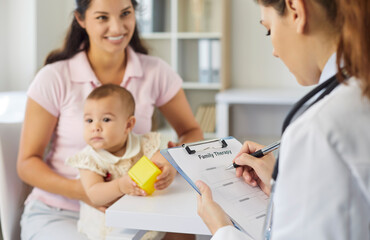 Fototapeta premium Pediatrician meets mother and baby for consultation. Family doctor reviews a therapy checklist on clipboard while infant patient plays with toy in medical clinic. Pediatric trust, care and medicine.
