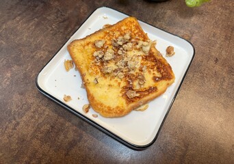 Slice of golden French toast topped with crumbs and crushed nuts. Perfect for bakery, brunch, or cozy breakfast photography