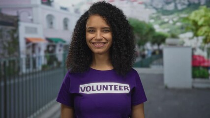 Smiling young woman volunteer in a purple shirt outdoors on a vibrant street illustrating community and youth engagement.