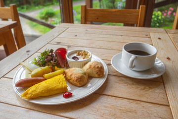 Healthy breakfast plate with omelette, croissants, salad, and coffee on wooden table