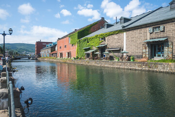 Historic canal with old warehouses and outdoor seating in sunny urban setting at Hokkaido, Japan