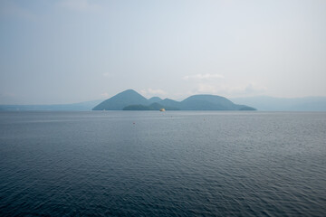 Calm sea with distant volcanic islands under hazy sky at Lake Toya, Abuta, Hokkaido, Japan